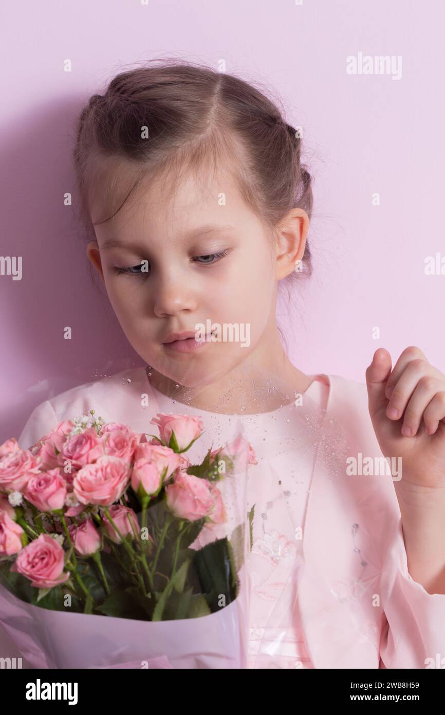 A cute little girl in a pink dress holds a bouquet of pink roses on a ...