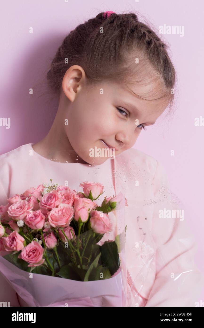 A cute little girl in a pink dress holds a bouquet of pink roses on a ...