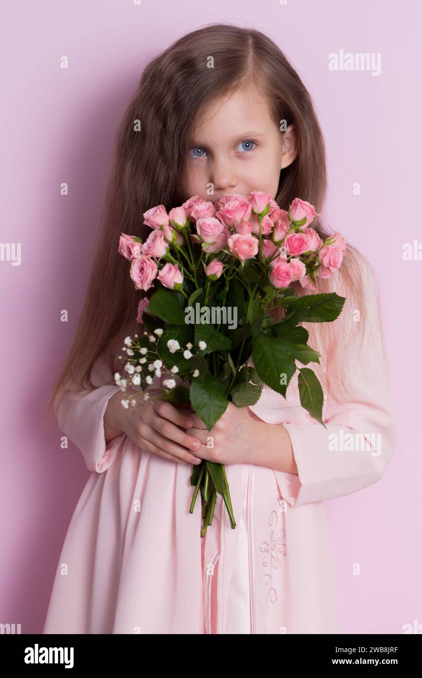 A cute little girl in a pink dress holds a bouquet of pink roses on a ...