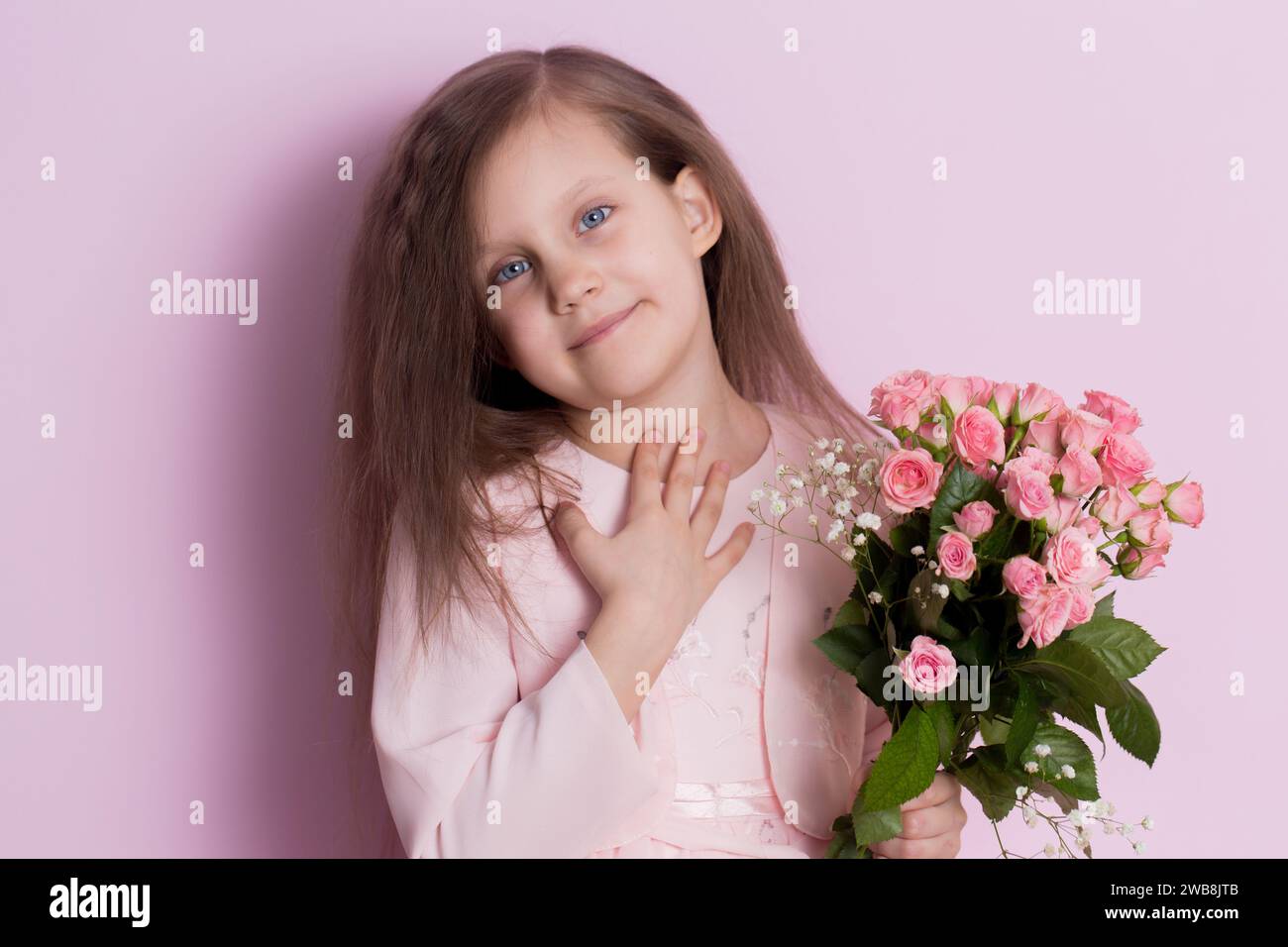 A cute little girl in a pink dress holds a bouquet of pink roses on a ...