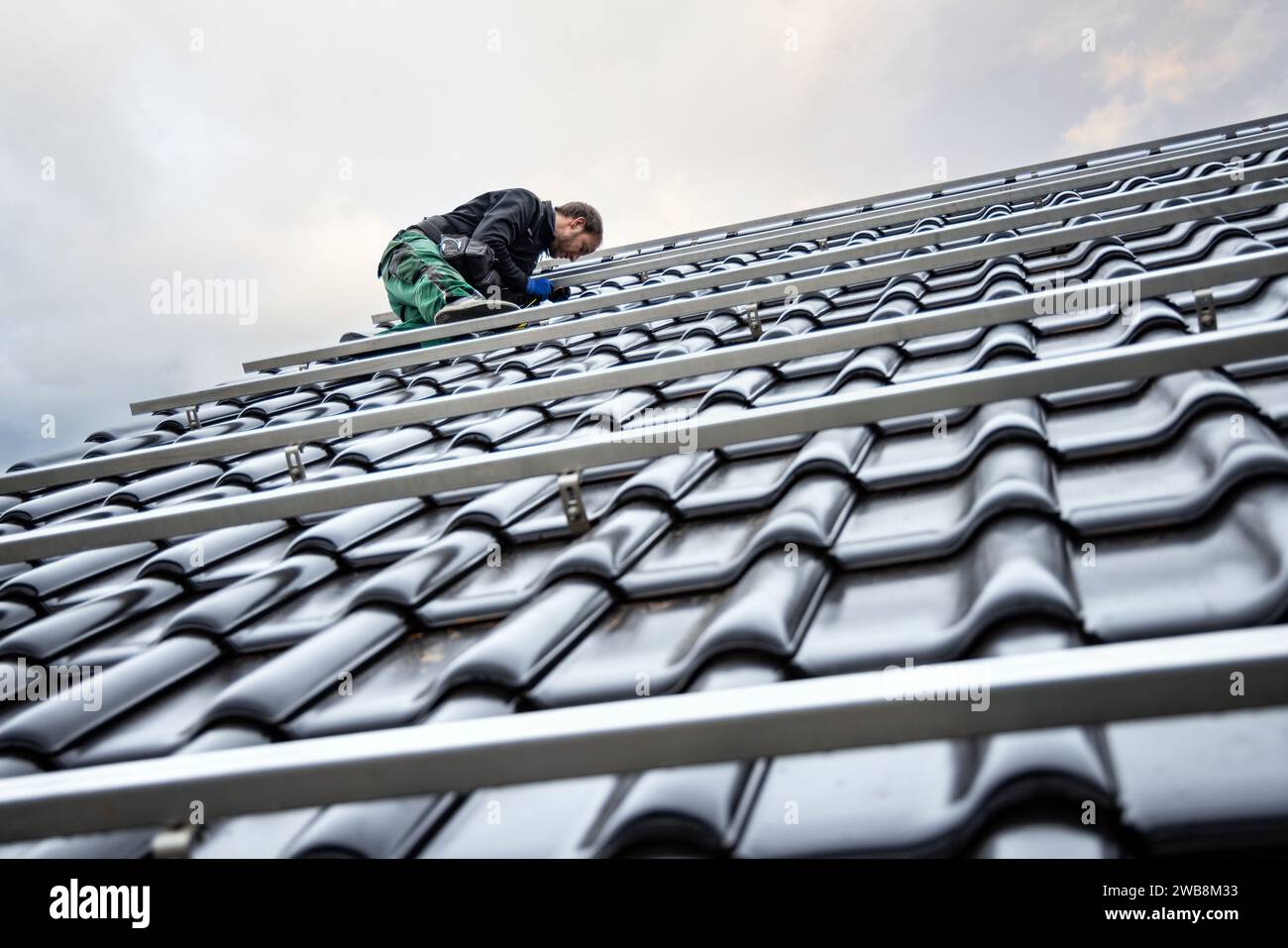 Technician on the Roof of a House Setting Up Mounting Structures for Solar Panels Stock Photo