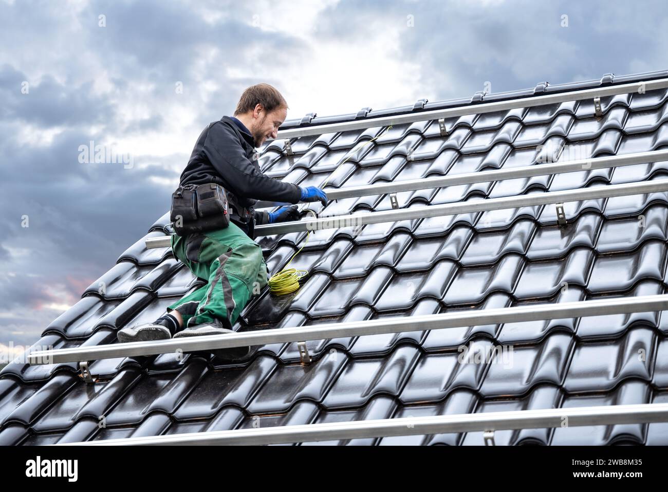 Man on the Rooftop of a House Setting Up the Mounting Structure for Solar Panels Stock Photo