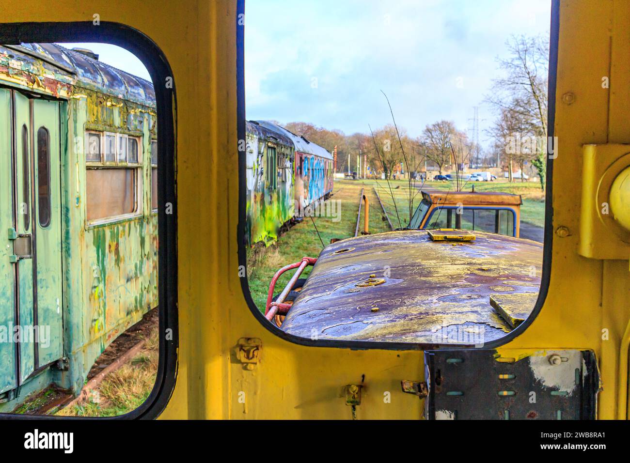 Panels in very old dismantled railway cockpit, metal corroded and rusted by passage of time, green passenger carriage seen through window in blurred b Stock Photo