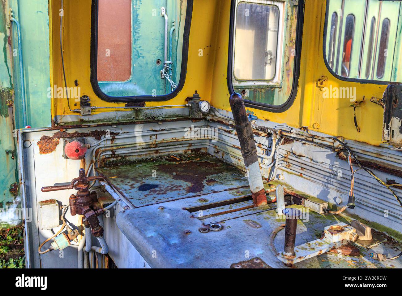 Interior of a very old dismantled railway cockpit, control levers, metal corroded and rusted by passage of time, windows, green passenger car in backg Stock Photo