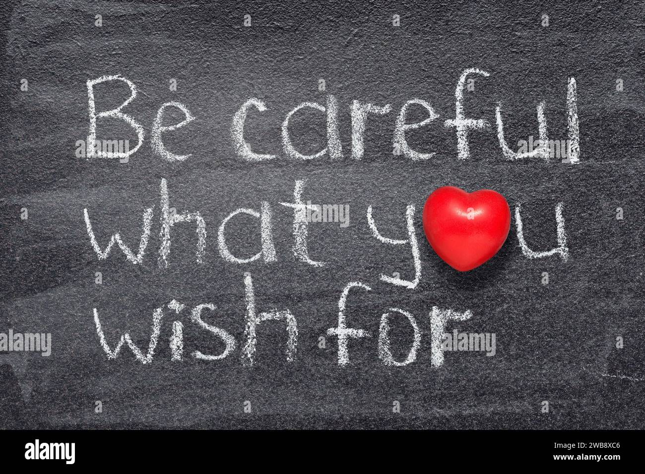 Be careful what you wish for saying written on chalkboard with red heart symbol Stock Photo