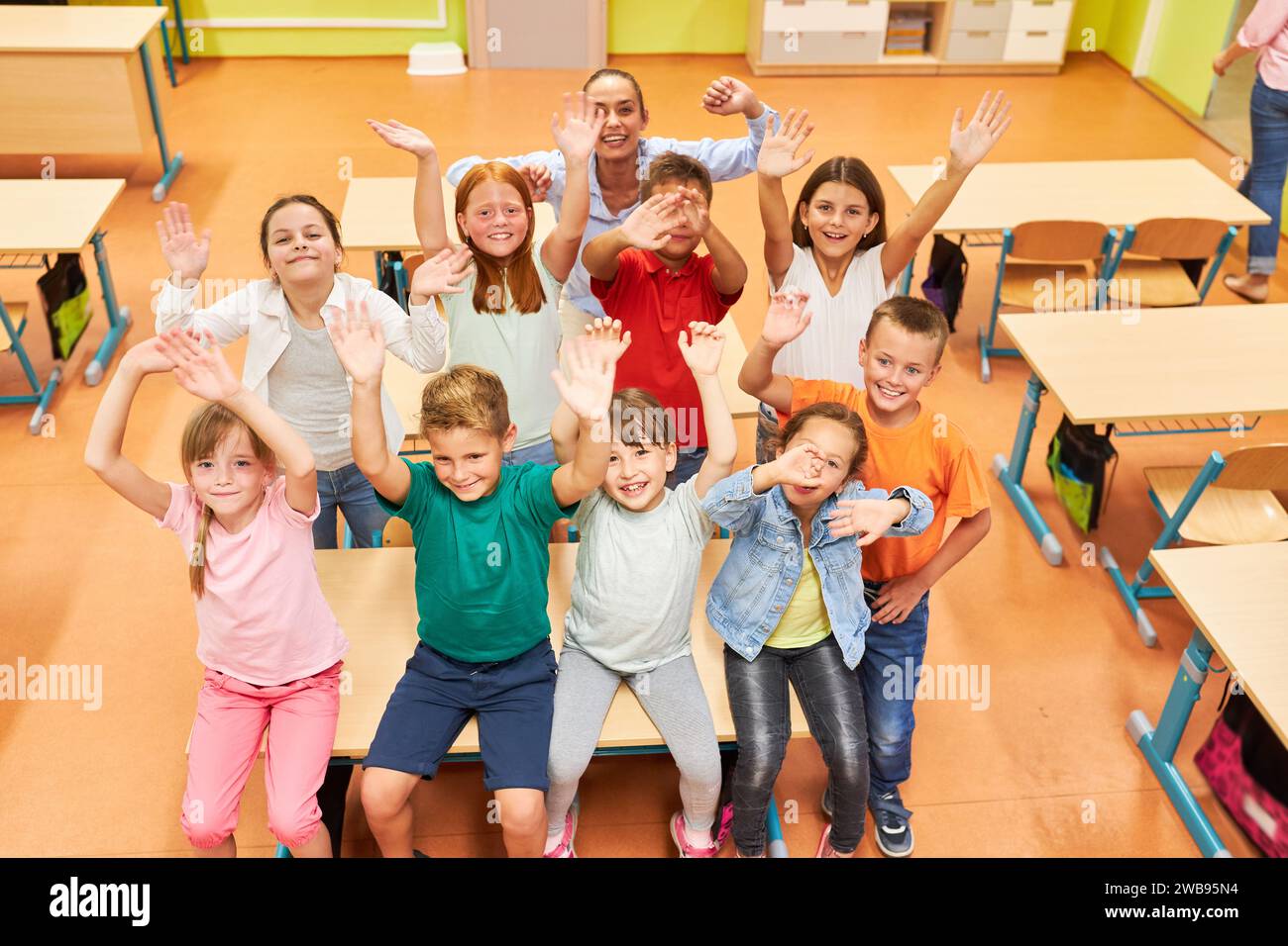 High angle view of happy male and female students waving with teacher in classroom at school Stock Photo