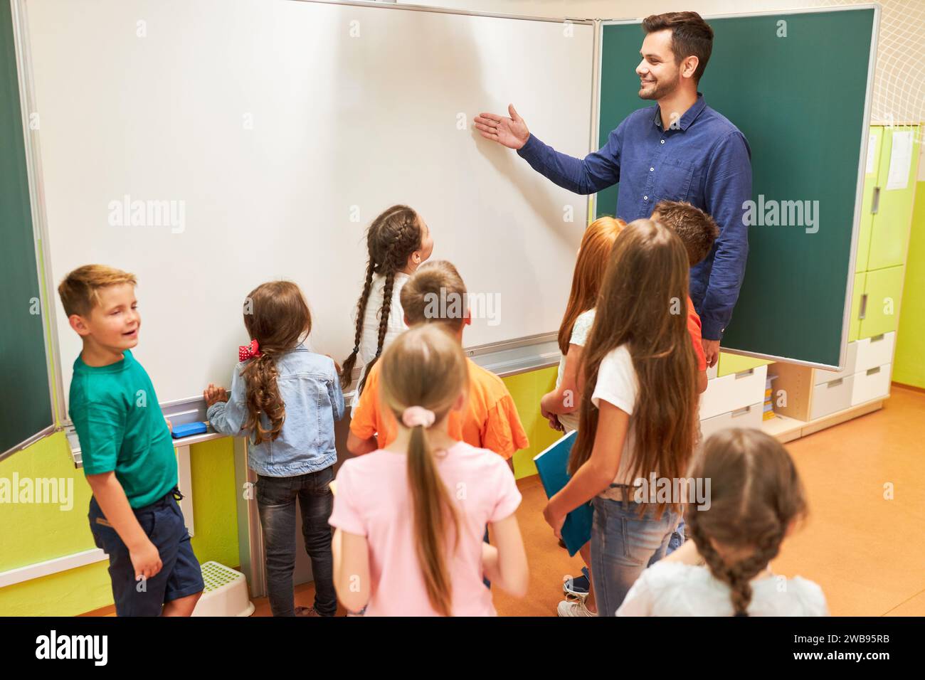 Smiling elementary teacher explaining students over whiteboard in classroom Stock Photo