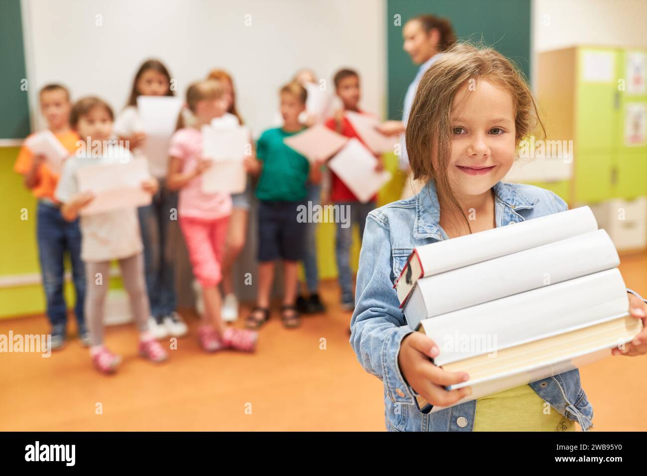 Portrait of smiling schoolgirl holding stack of books while standing in classroom Stock Photo