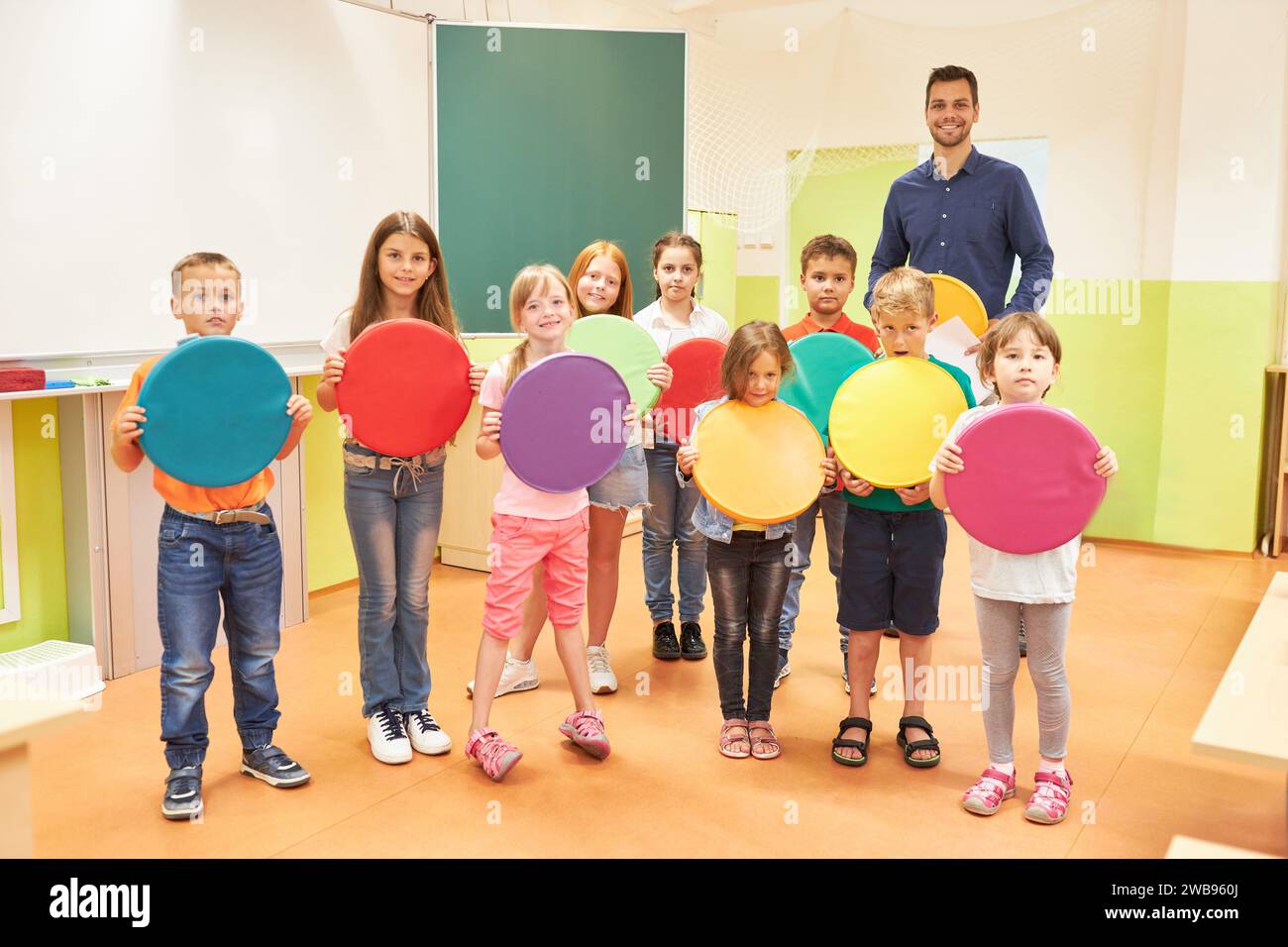 Group of elementary students holding circle shaped seat cushions while standing with teacher in classroom Stock Photo