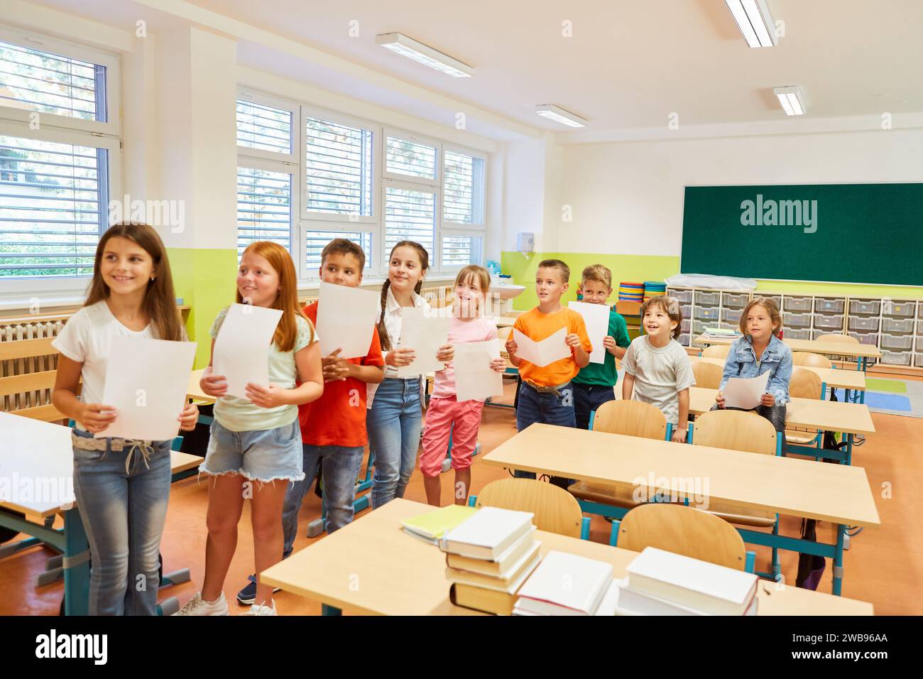 Group of smiling school students standing in row holding paper during activity in classroom Stock Photo