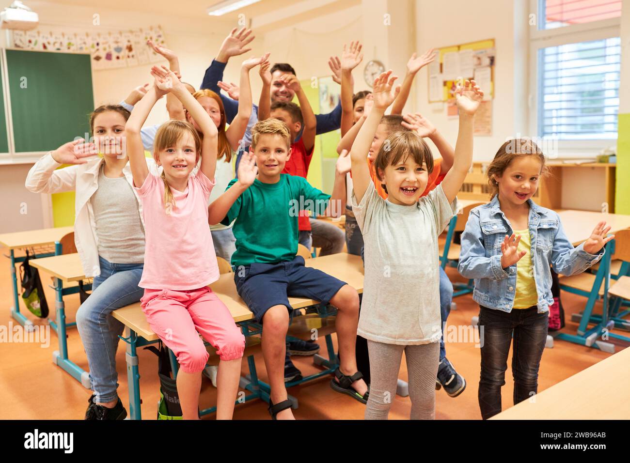 Group of male and female elementary students waving in classroom at school Stock Photo