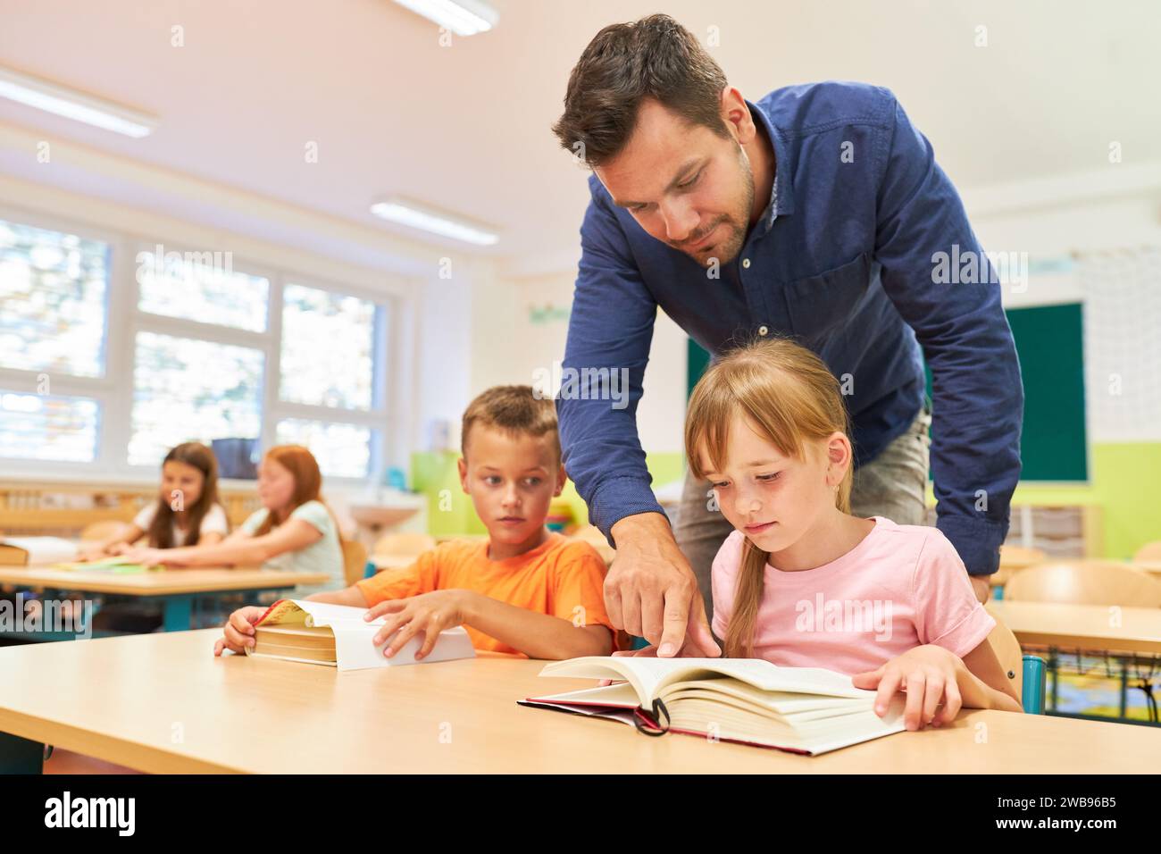 Male teacher helping student while reading book on bench in classroom
