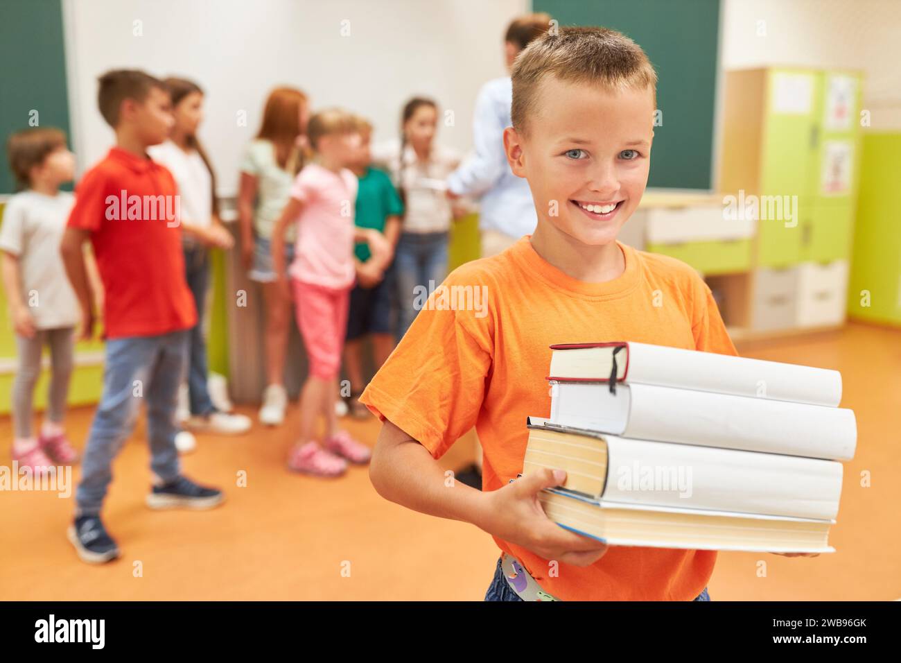 Portrait of smiling schoolboy holding stack of books while standing in class Stock Photo