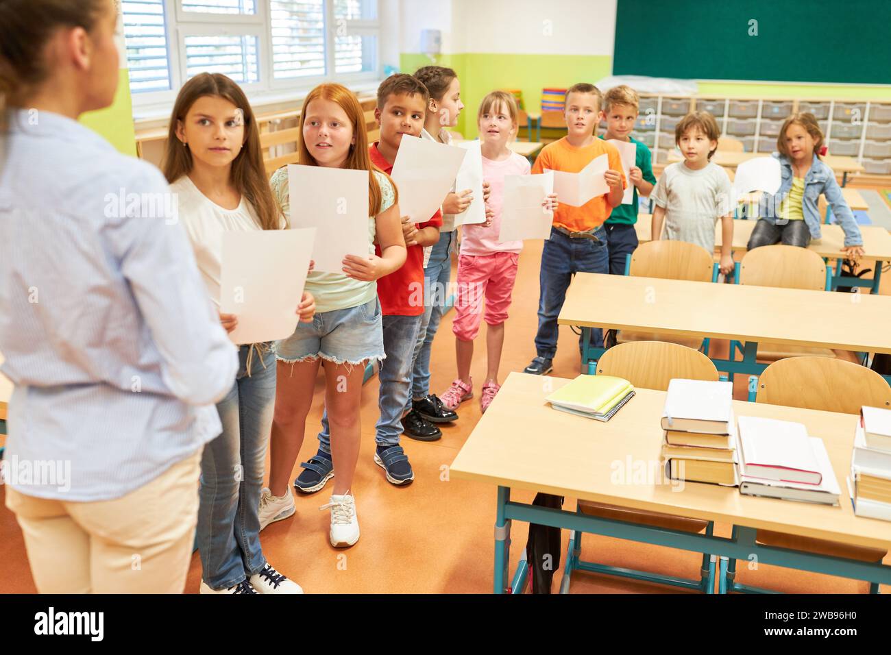 Schoolkids standing in row and doing choir rehearsal with teacher in class at school Stock Photo