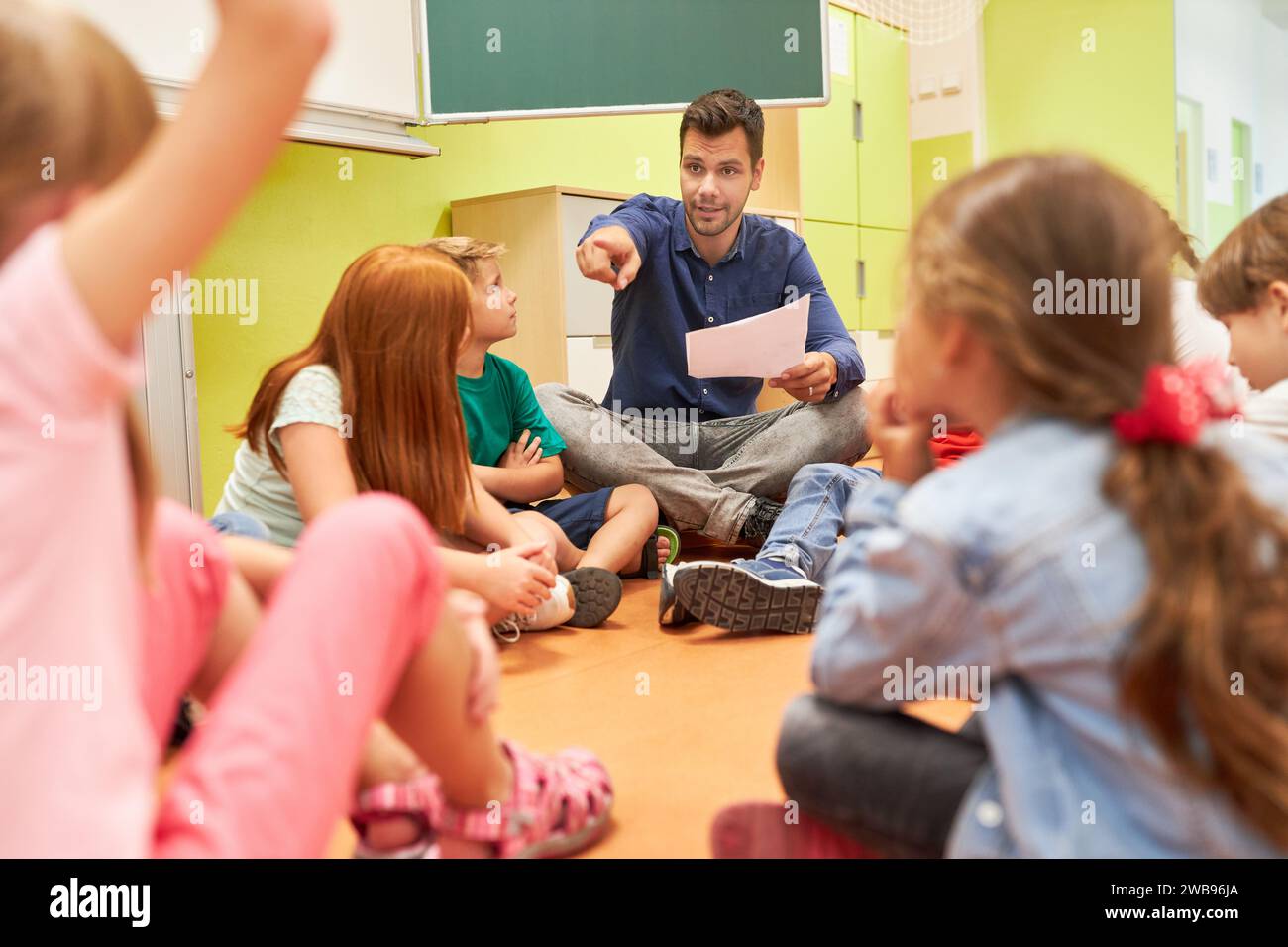 Elementary school teacher sitting in circle with group of students in classroom Stock Photo