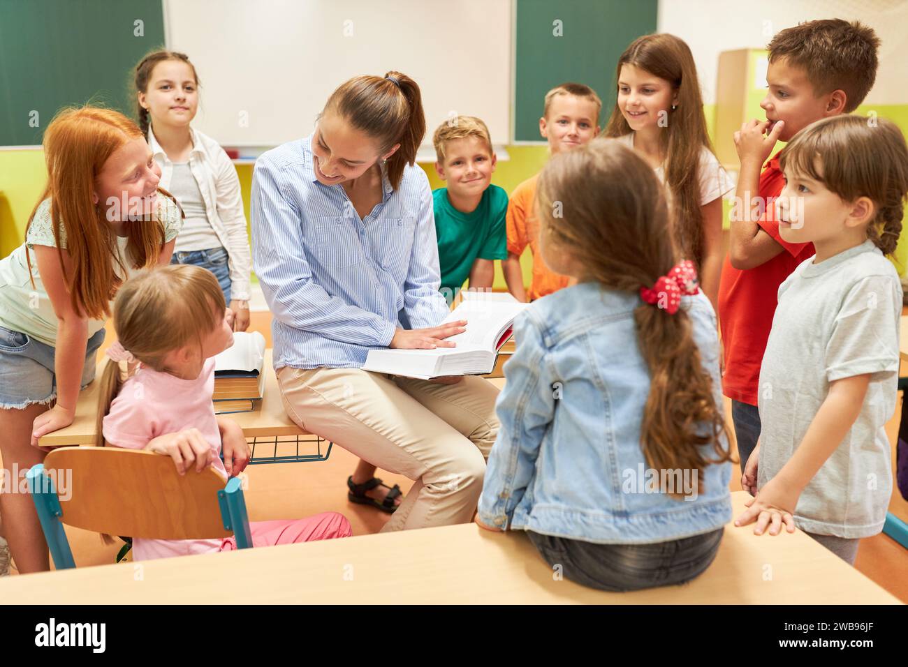 Elementary Female Teacher Talking With Schoolkids Sitting On Bench In Elementary Female Teacher Talking With Schoolkids Sitting On Bench In