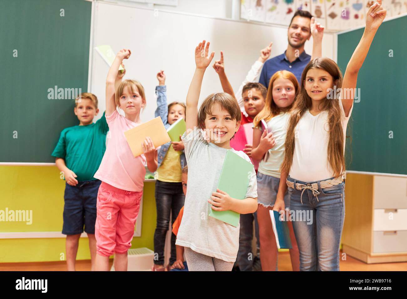 Group of happy school kids raising hands in classroom Stock Photo