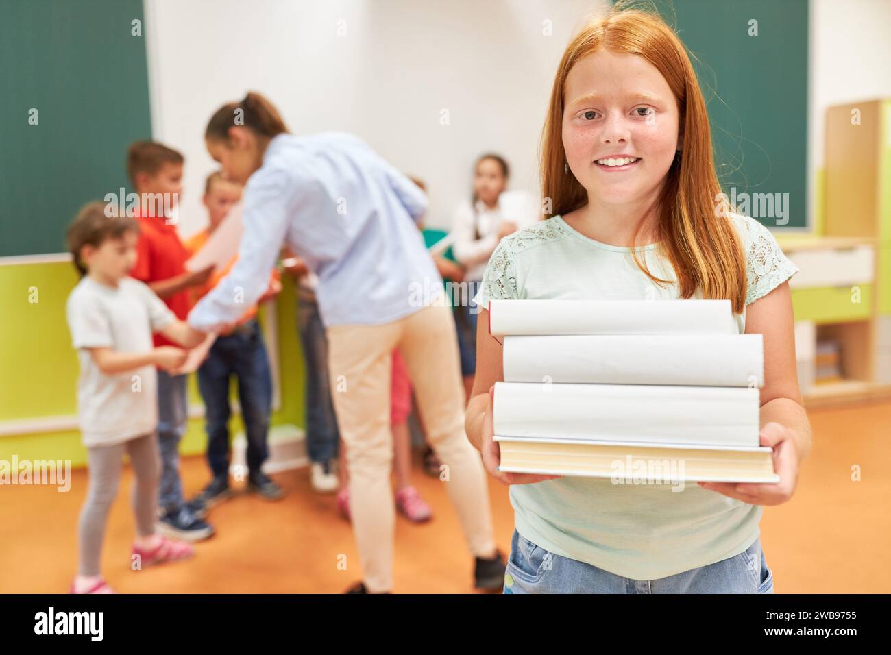 Portrait of smiling redhead schoolgirl holding stack of books while standing in class Stock Photo