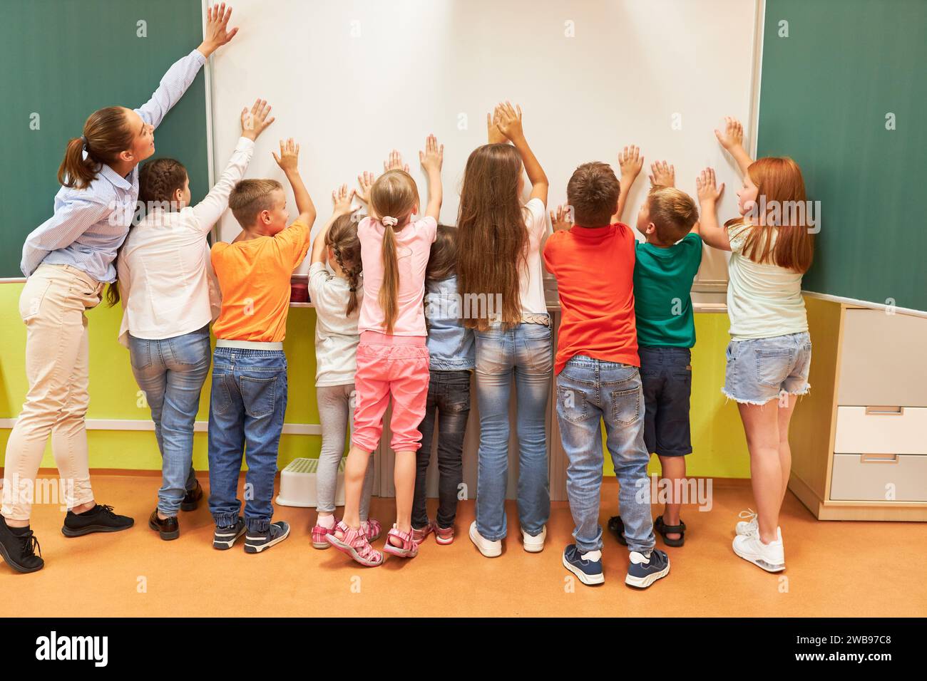 Rear view full length of students touching whiteboard with female teacher in classroom Stock Photo