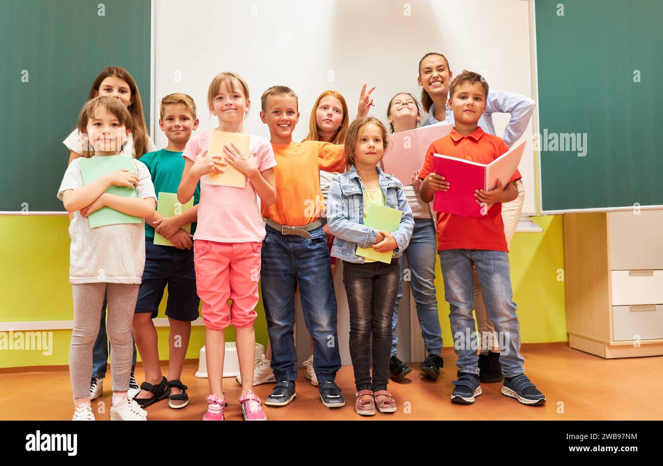 Group of happy school kids posing with female teacher in class Stock Photo