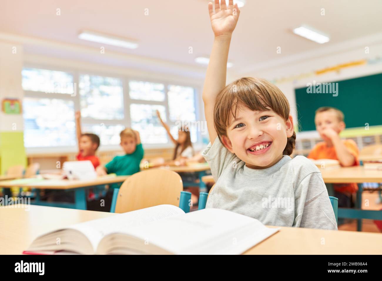 Portrait of smiling schoolgirl sitting with hand raised on bench during lecture in classroom Stock Photo