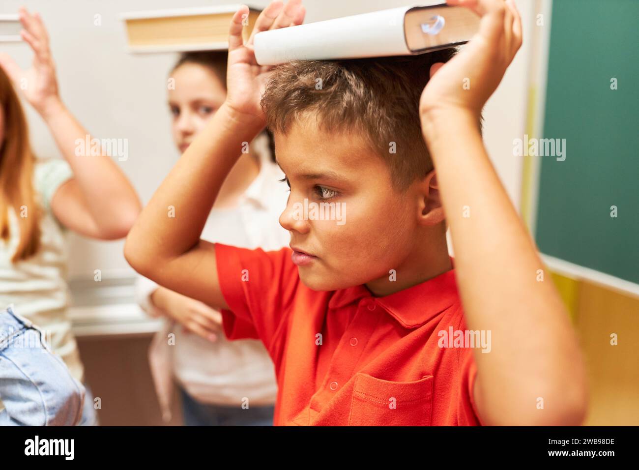 Schoolboy balancing book on head during activity in classroom at school Stock Photo