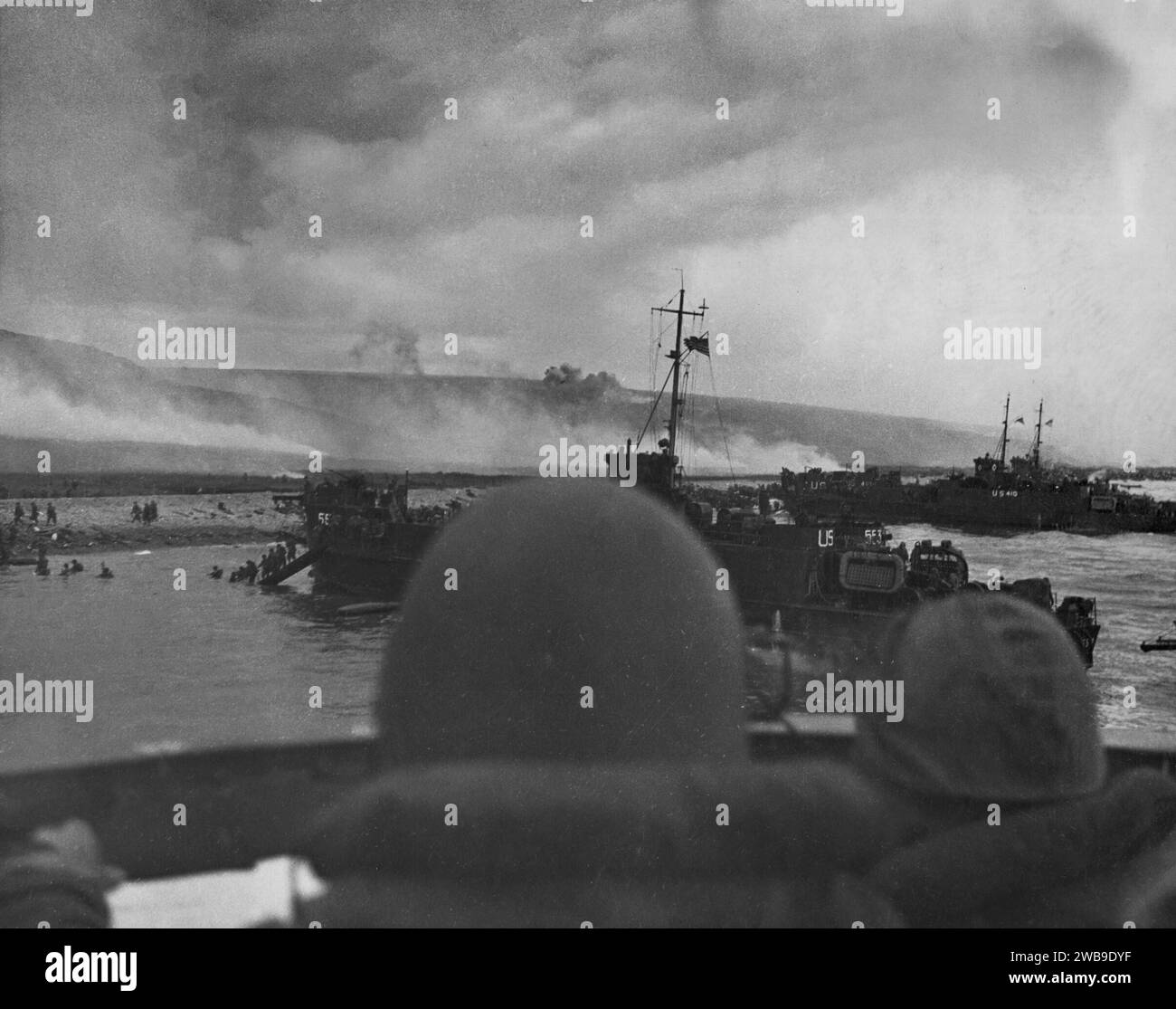 OMAHA BEACH, NORMANDY, FRANCE - 06 June 1944 - Two US Navy sailors (foreground) navigate near Omaha Beach during the early stages of the Invasion of N Stock Photo