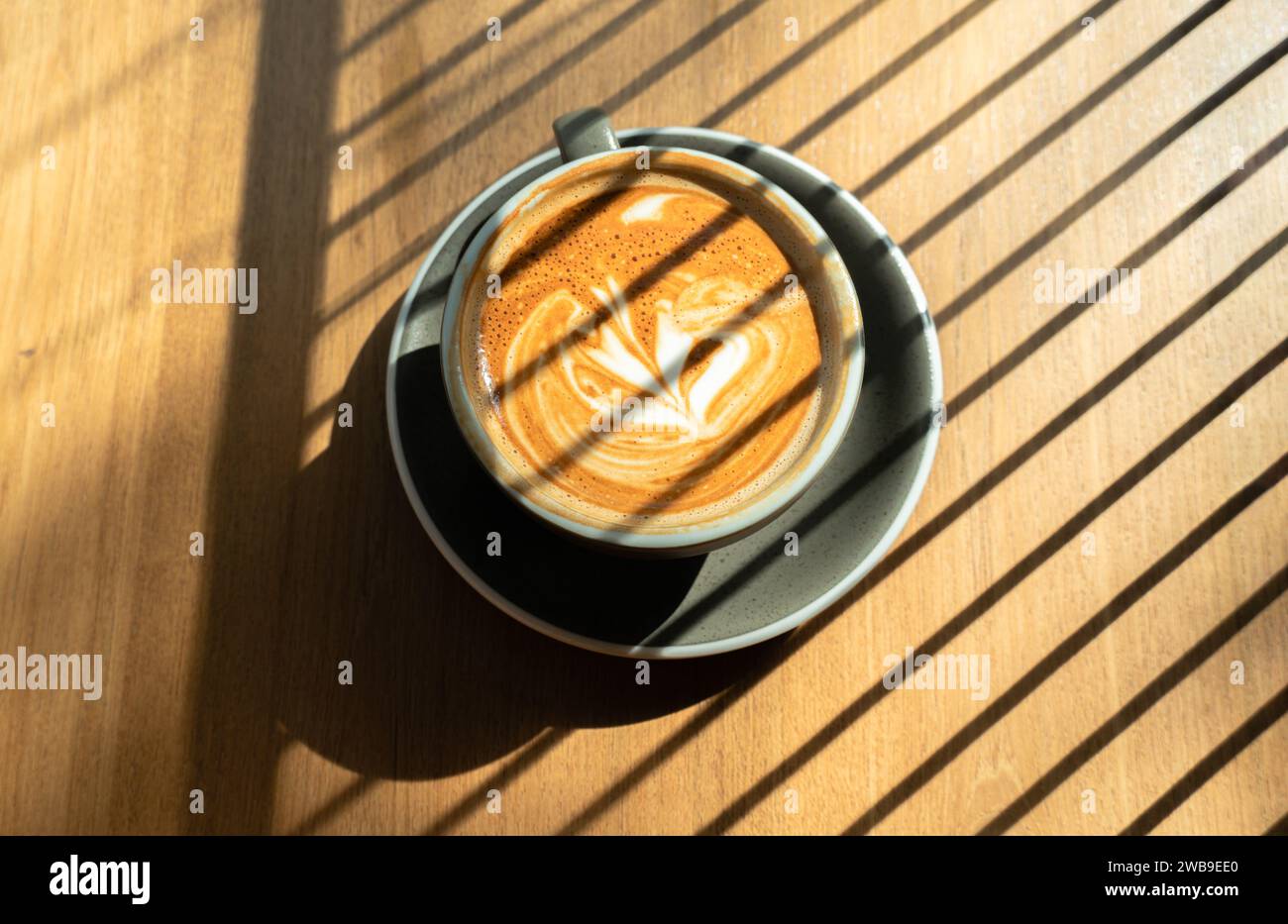 Late coffee art on the wooden table. relaxation concept. Iced coffee latte with soft white milk foam and sunlight shining through. Photograph of a cup Stock Photo