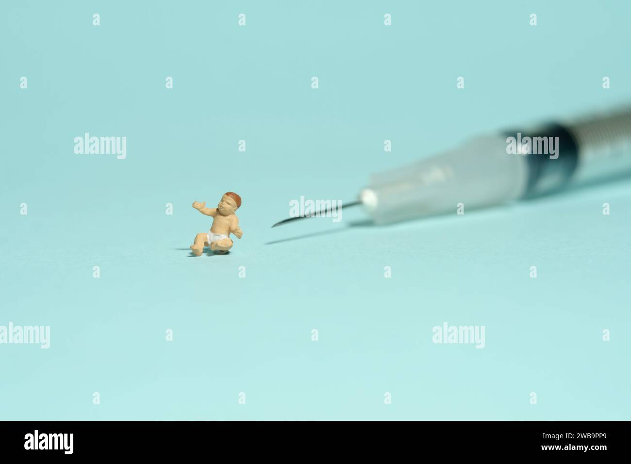 Miniature tiny people toy figure photography. A boy toddler infant baby seat in front of needle syringe. Isolated on blue background. Image photo Stock Photo