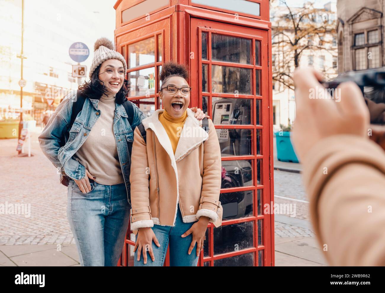 two friend, girlfriend, women using  camera and taking photos against a red phonebox in the city of England.Travel Lifestyle concept Stock Photo