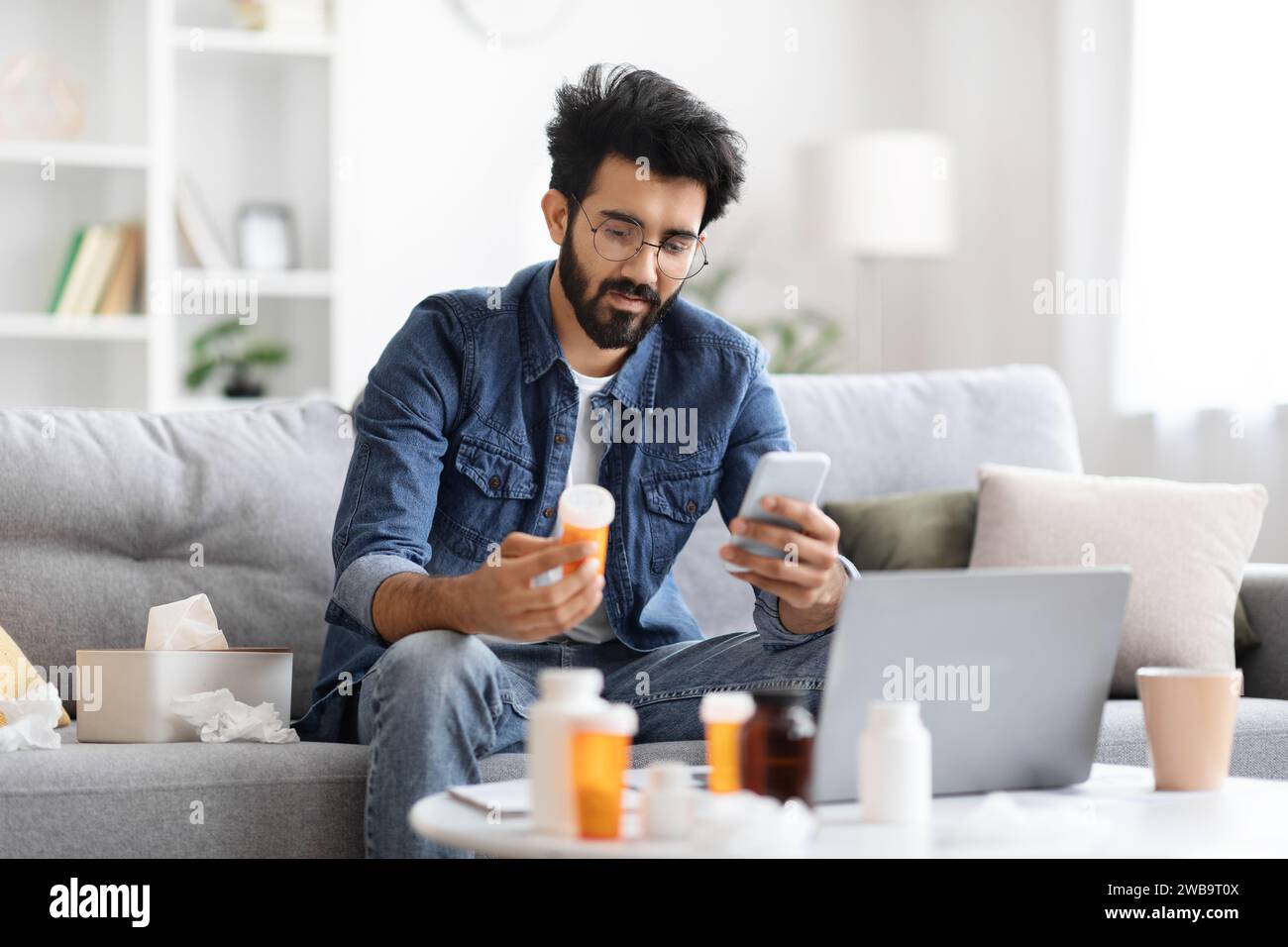 Young indian man holding bottle with pills and using smartphone Stock Photo