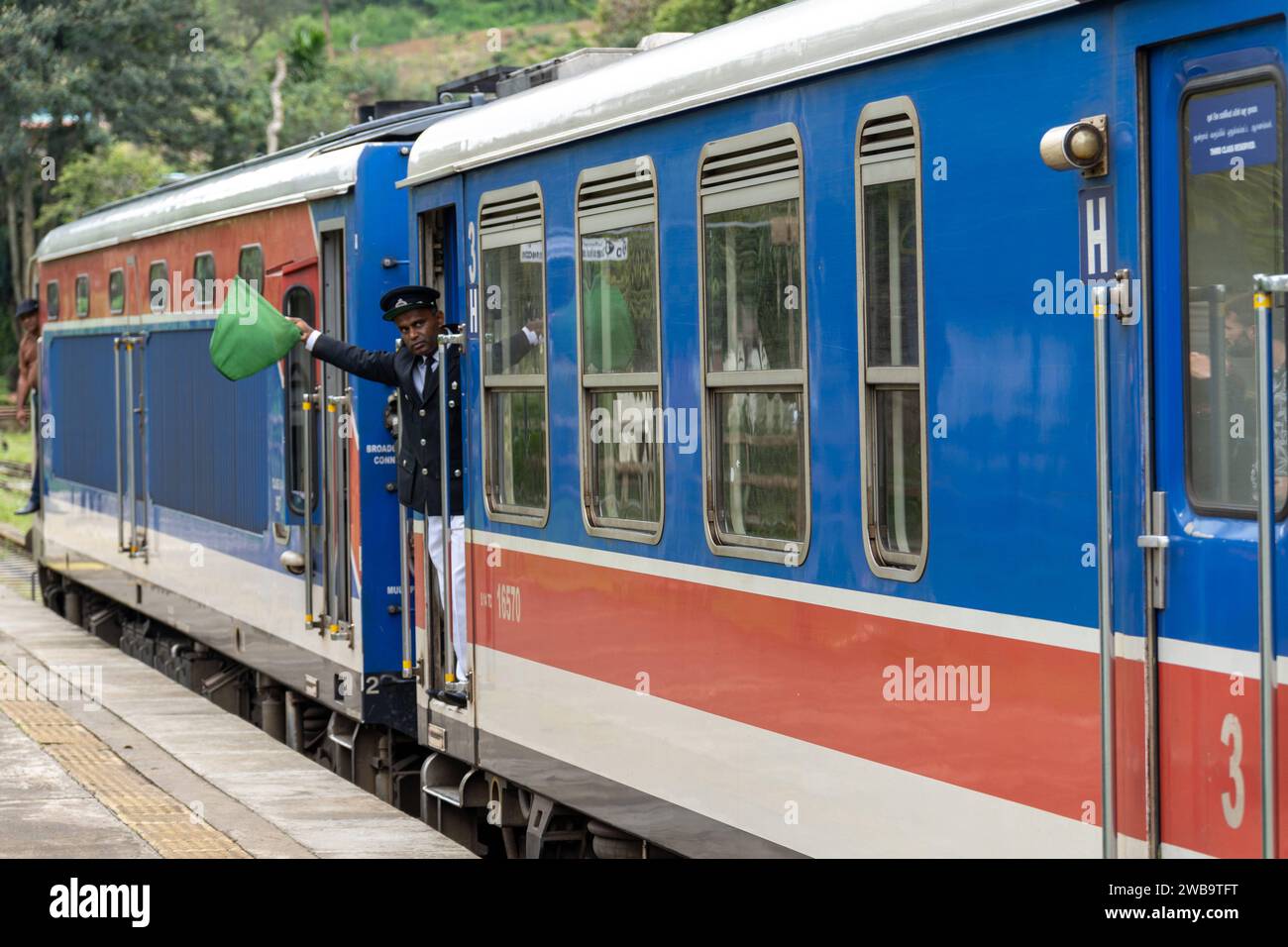 Ella, Sri Lanka, Asia - December 19, 2023: Ella train station in Sri Lanka. A conductor waves for the departure of a train *** Bahnhof von Ella auf Sri Lanka. Ein Schaffner winkt zur Abfahrt von einem Zug Stock Photo