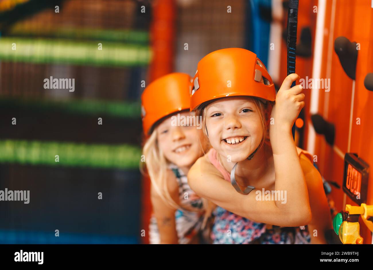 Two happy school girls in sports helmets at climbing class. Indoor bouldering class for school children. Kids enjoy at amusement park Stock Photo