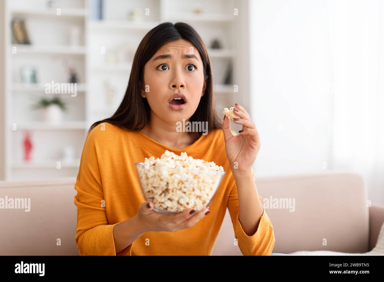 Closeup frightened young asian woman watching scary movie at home Stock Photo