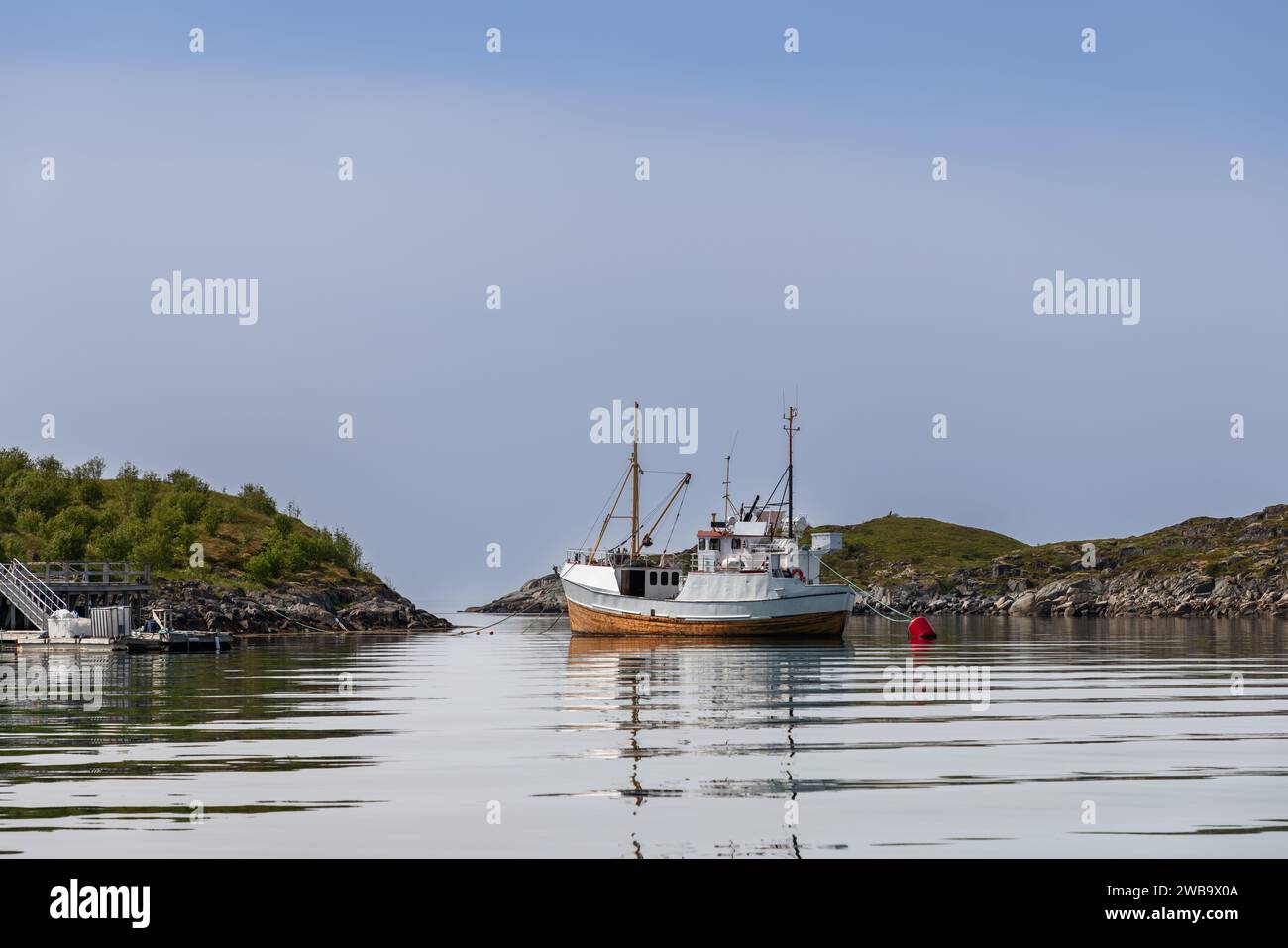 Quietude envelops a Lofoten inlet, with a solitary fishing boat anchored, reflecting on the water's glassy surface. Norway Stock Photo