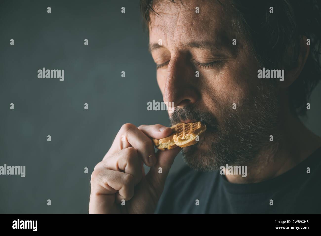 Adult man eating homemade cookie while standing by the window in morning, selective focus Stock Photo