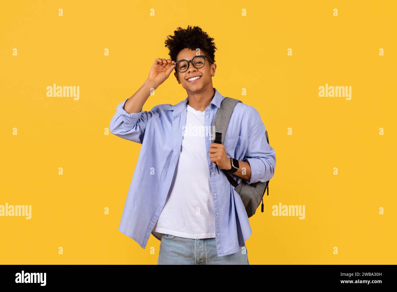 Confident black student adjusting glasses on a yellow background Stock Photo