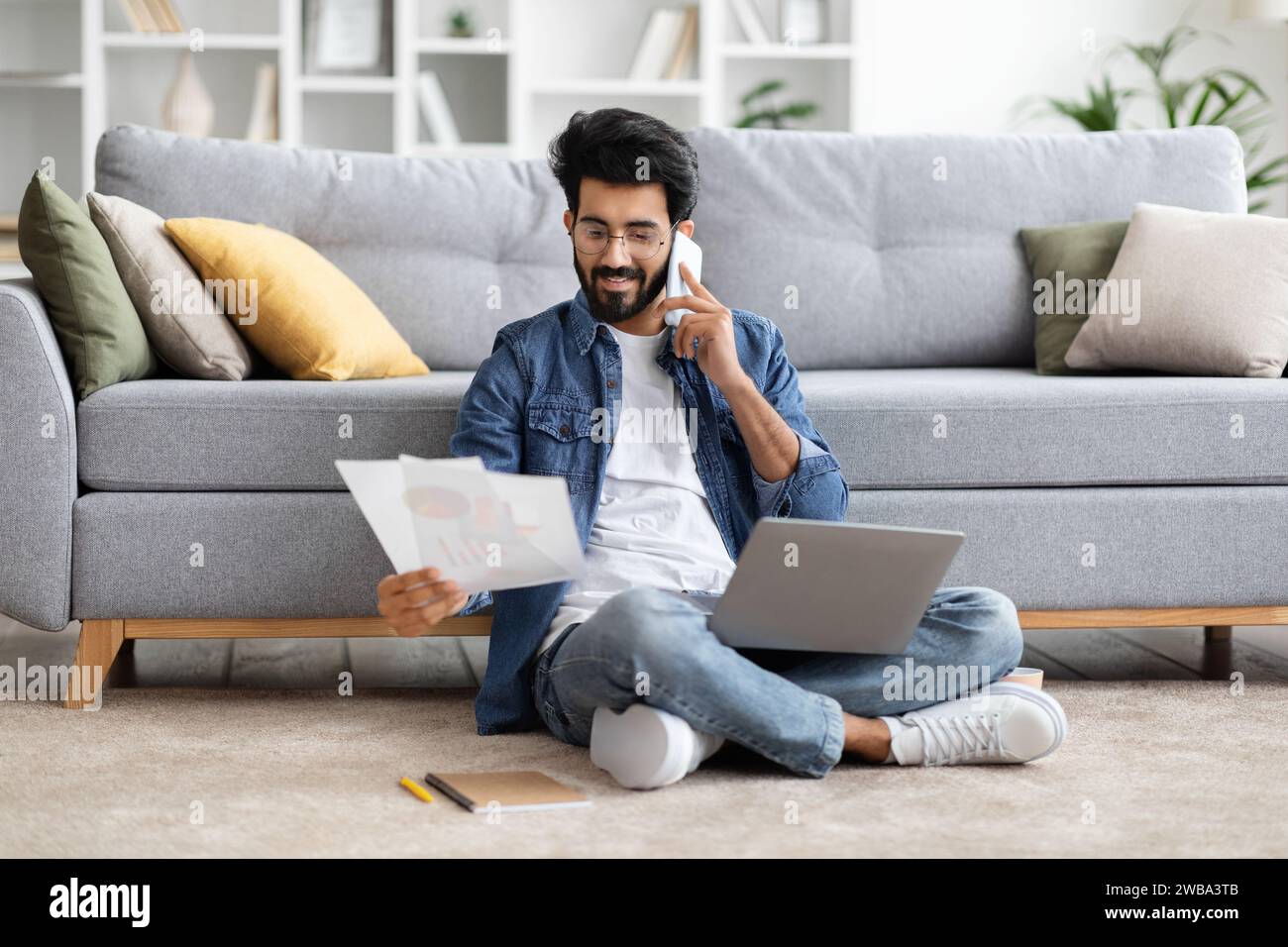 Focused indian man working from home, talking on phone and analyzing documents Stock Photo