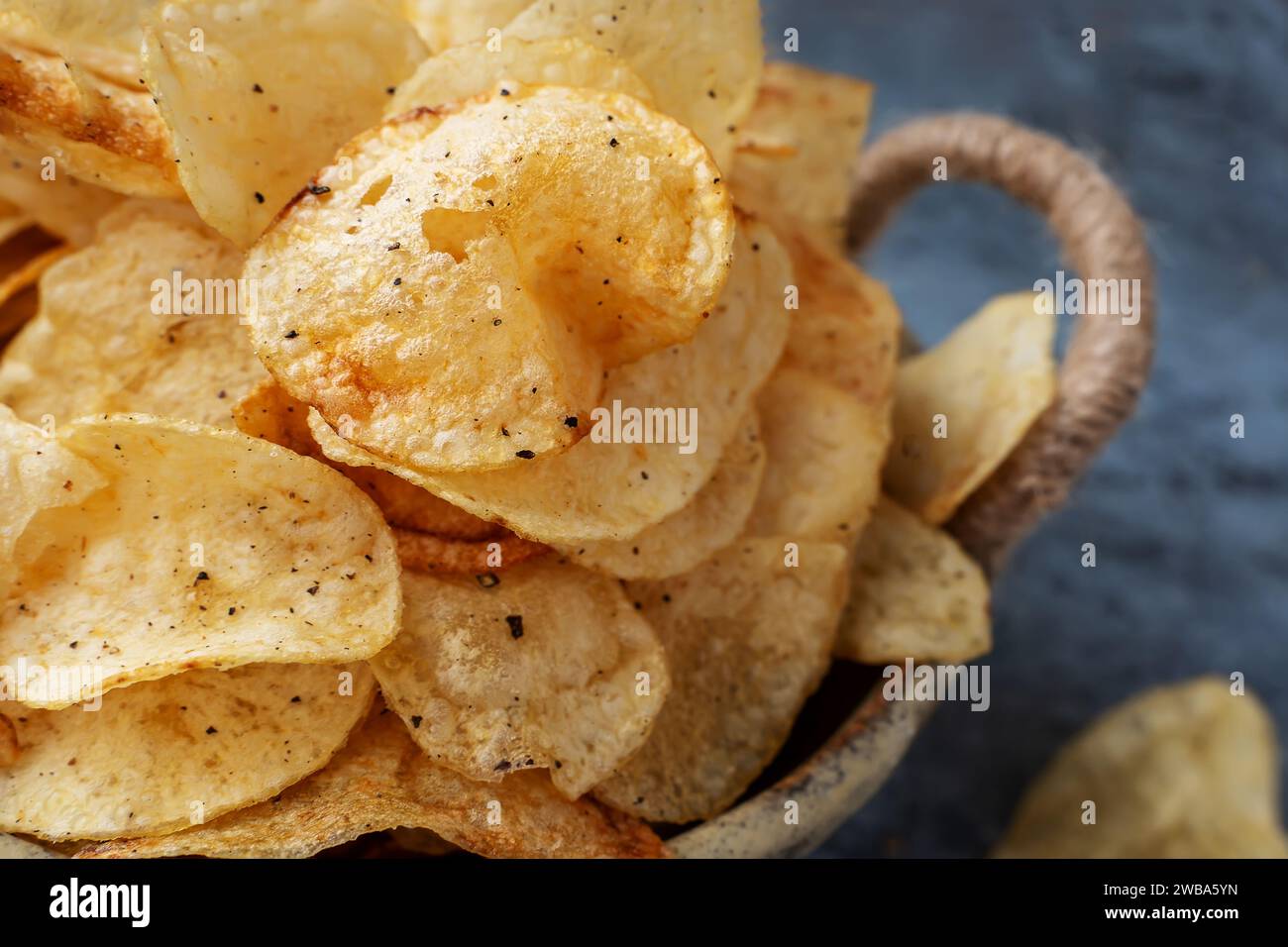 Savory chips in a handmade kraft bowl on a gray background. Potato chips with spices and peppers of different kinds. Close-up. Stock Photo