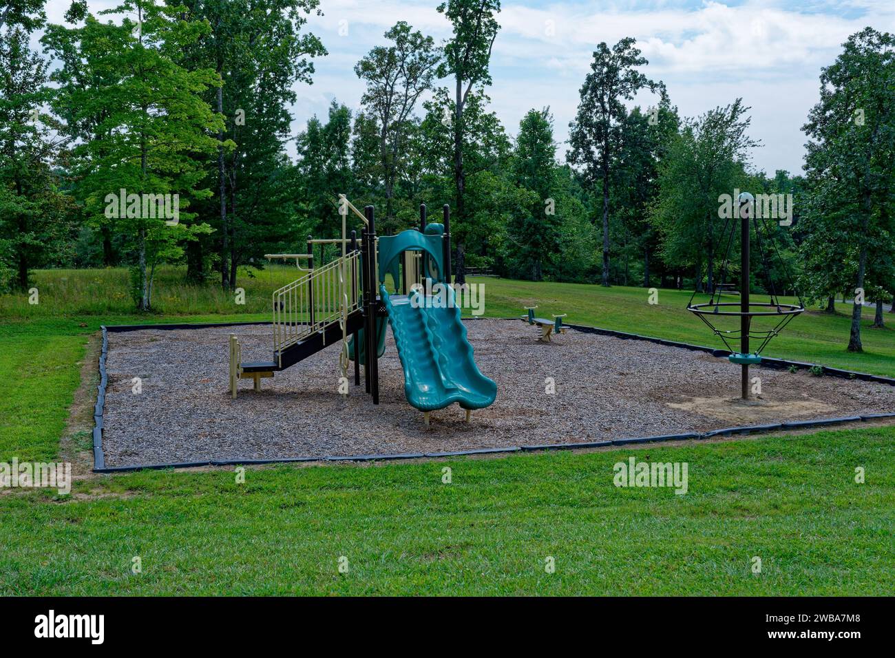 New and clean playground equipment in a empty public park with a forest in the background in late summertime Stock Photo