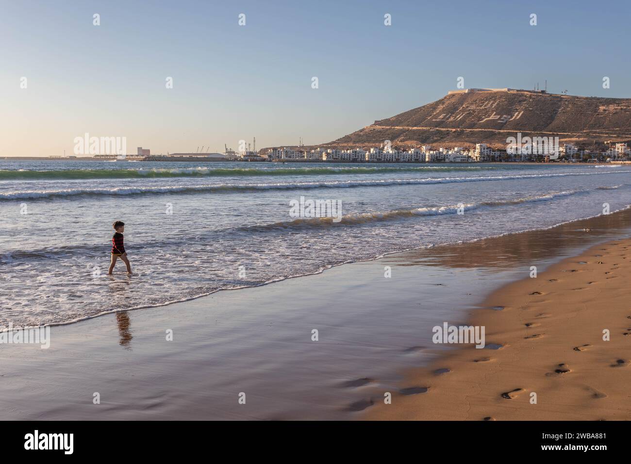 Child paddling in ocean as the sun sets on the beach in Agadir, Morocco, North Africa Stock Photo