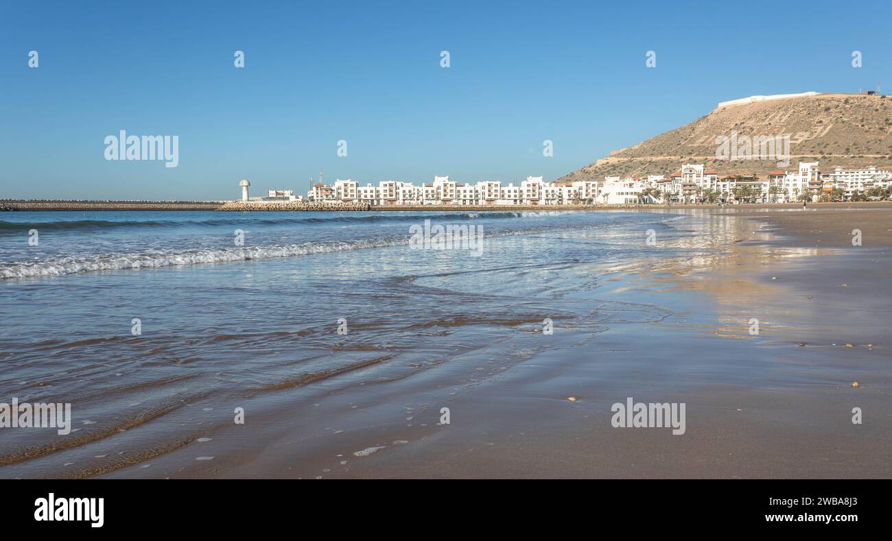 Agadir Beach and tide of Atlantic Ocean, with Kasbah and Marina in the distance Stock Photo