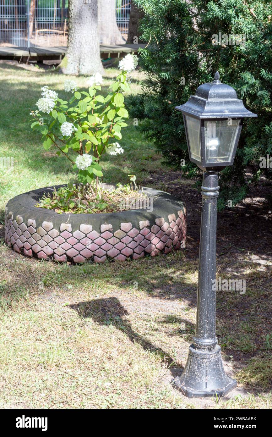 A garden light pole with a tractor tire as a flowerbed in the background Stock Photo