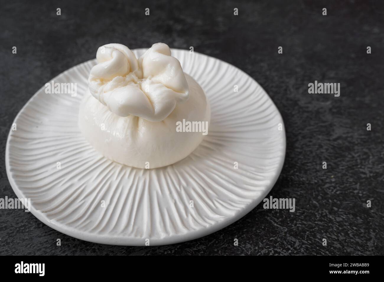 burrata on a beautiful handmade white plate. The dish is set against a dark background, copy space. Stock Photo