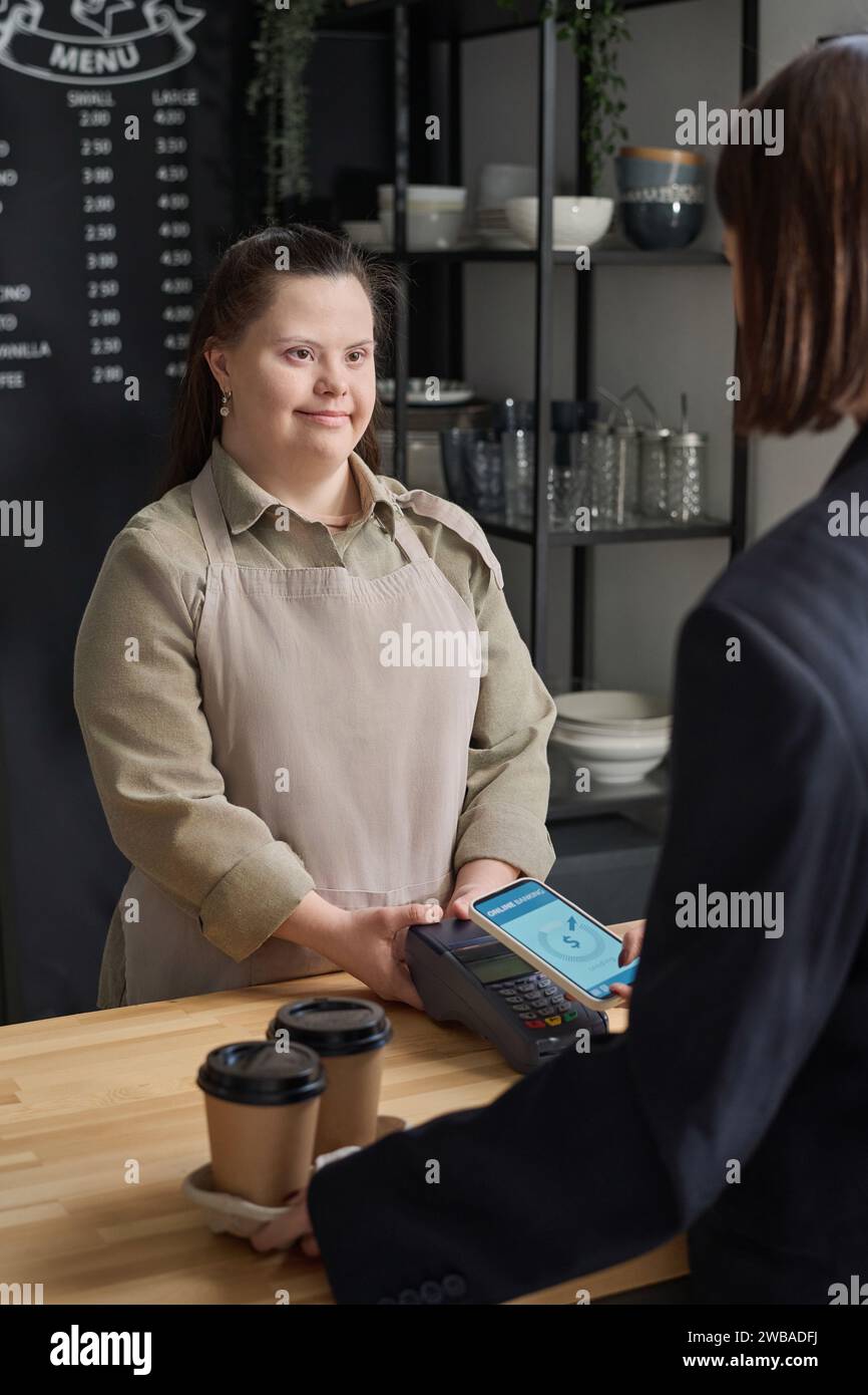 Young waitress with Down syndrome looking at guest of cafe paying for