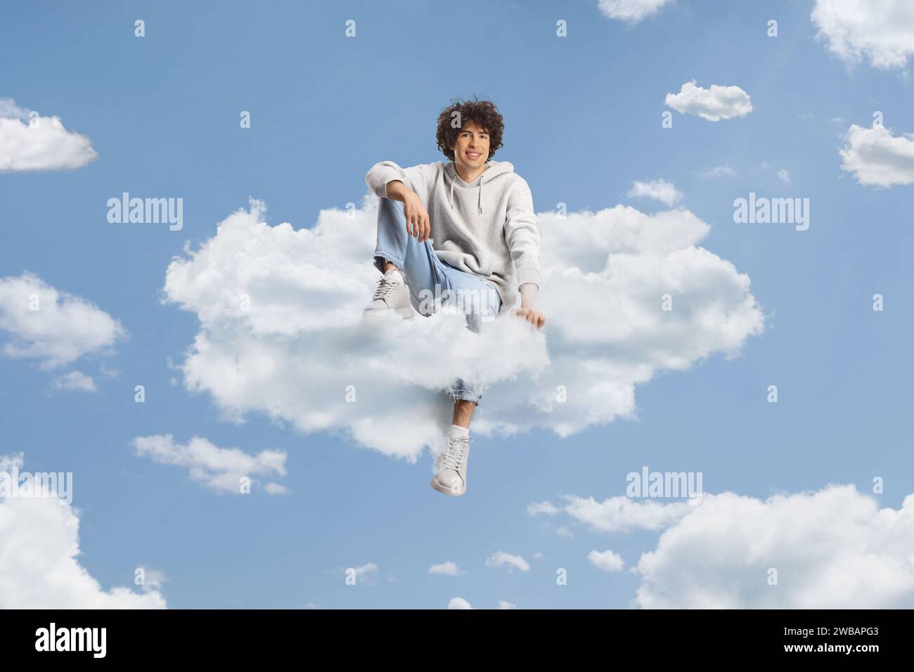 Guy with curly hair sitting on a cloud and smiling in the blue sky Stock Photo