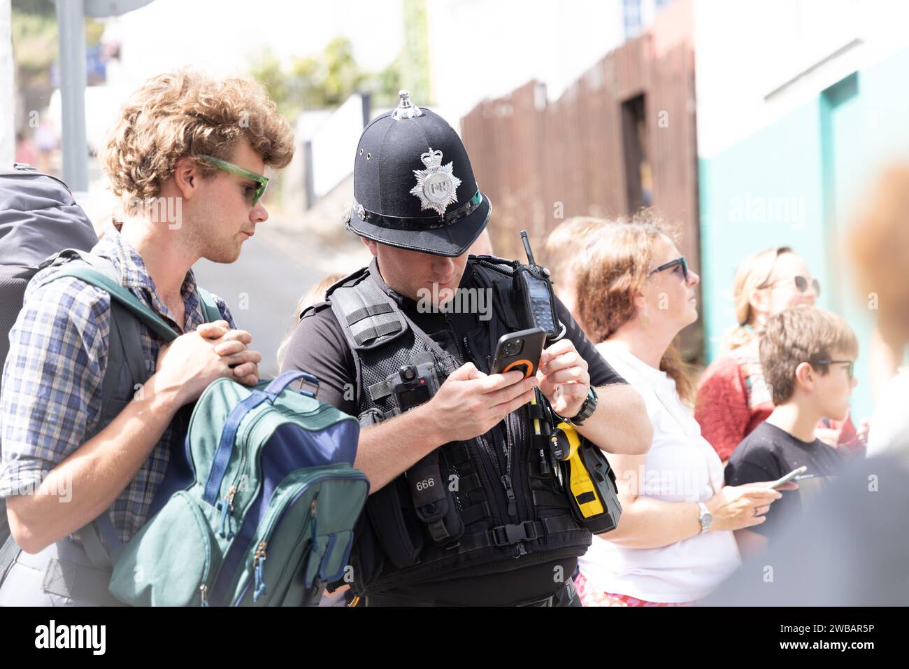 Policeman helping person in street by looking up information on phone for a bystander Stock Photo