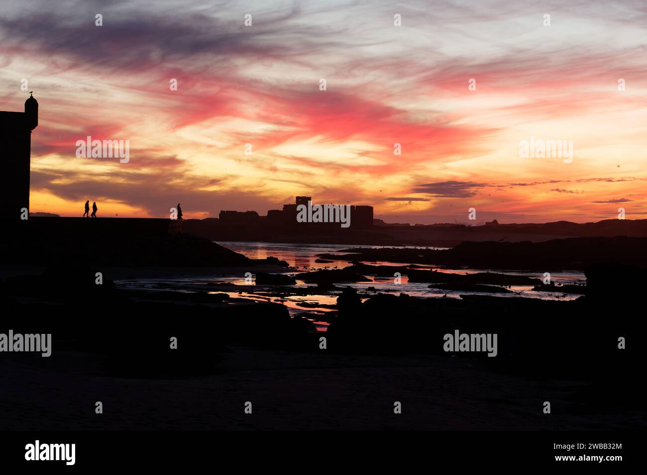 Dramatic sunset over the rocky coastline and fort area as people in silhouette stands on the city walls, in Essaouira, Morocco. 9th Jan 2024 Stock Photo