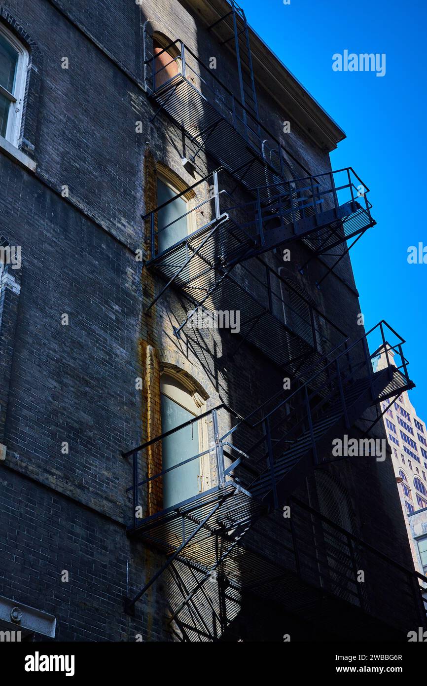 Urban Fire Escape Shadows on Brick Facade with Blue Sky Background Stock Photo