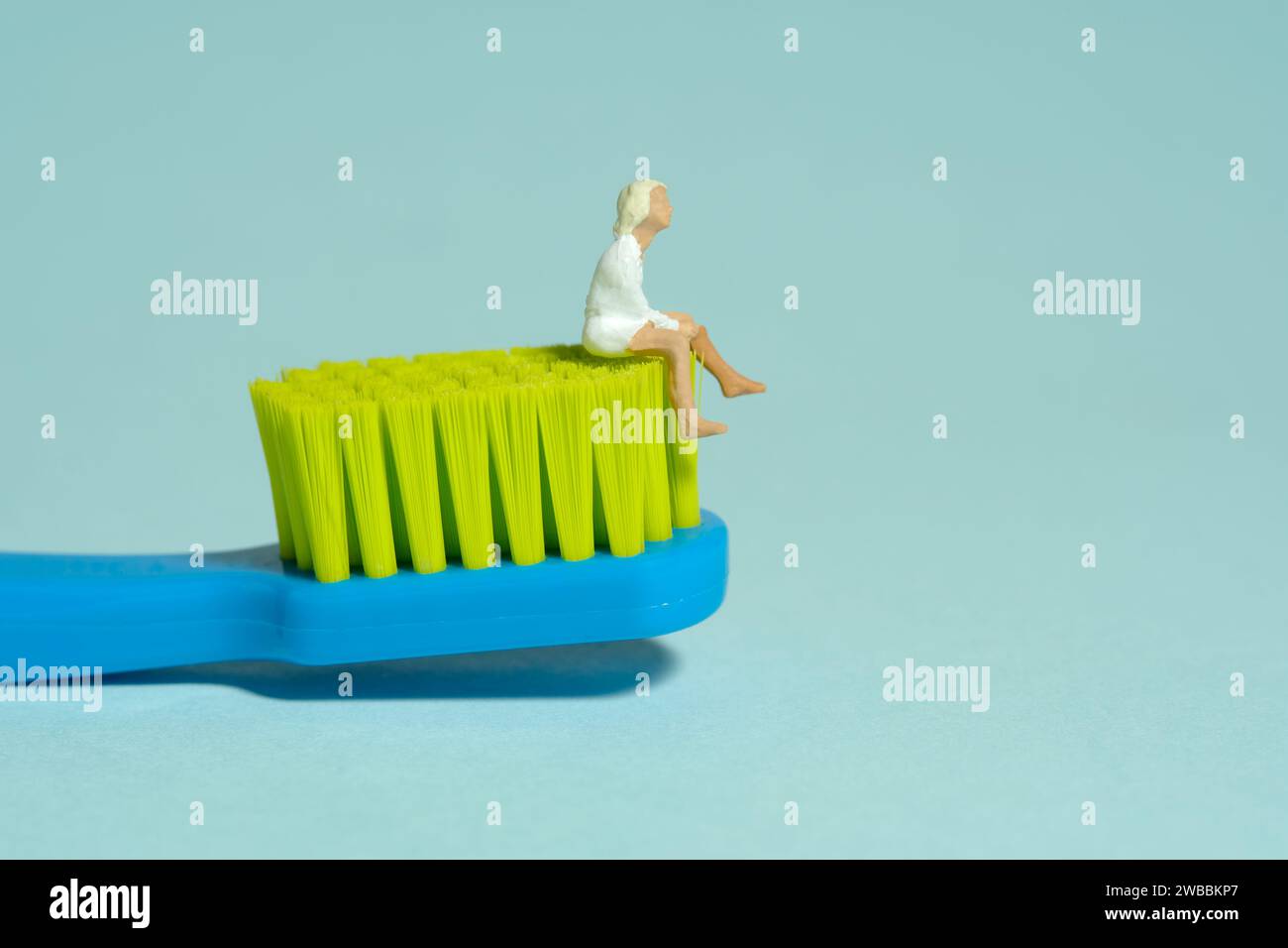 Miniature tiny people toy figure photography. A girl teenager sitting above toothbrush. Isolated on blue background. Image photo Stock Photo